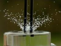 Wibrujący kamerton włożony do szklanki z wodą w slow motion.
